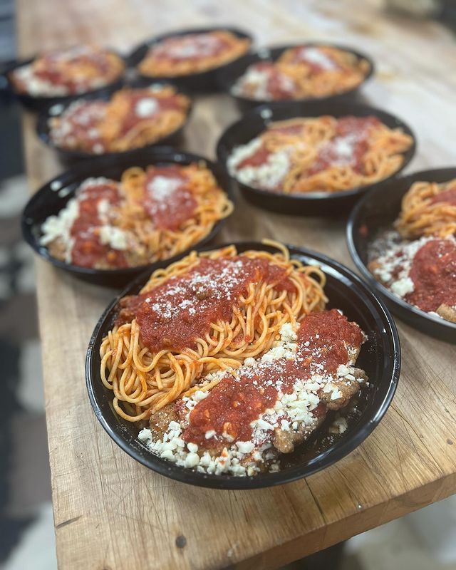 A wooden table topped with bowls of spaghetti and meatballs.