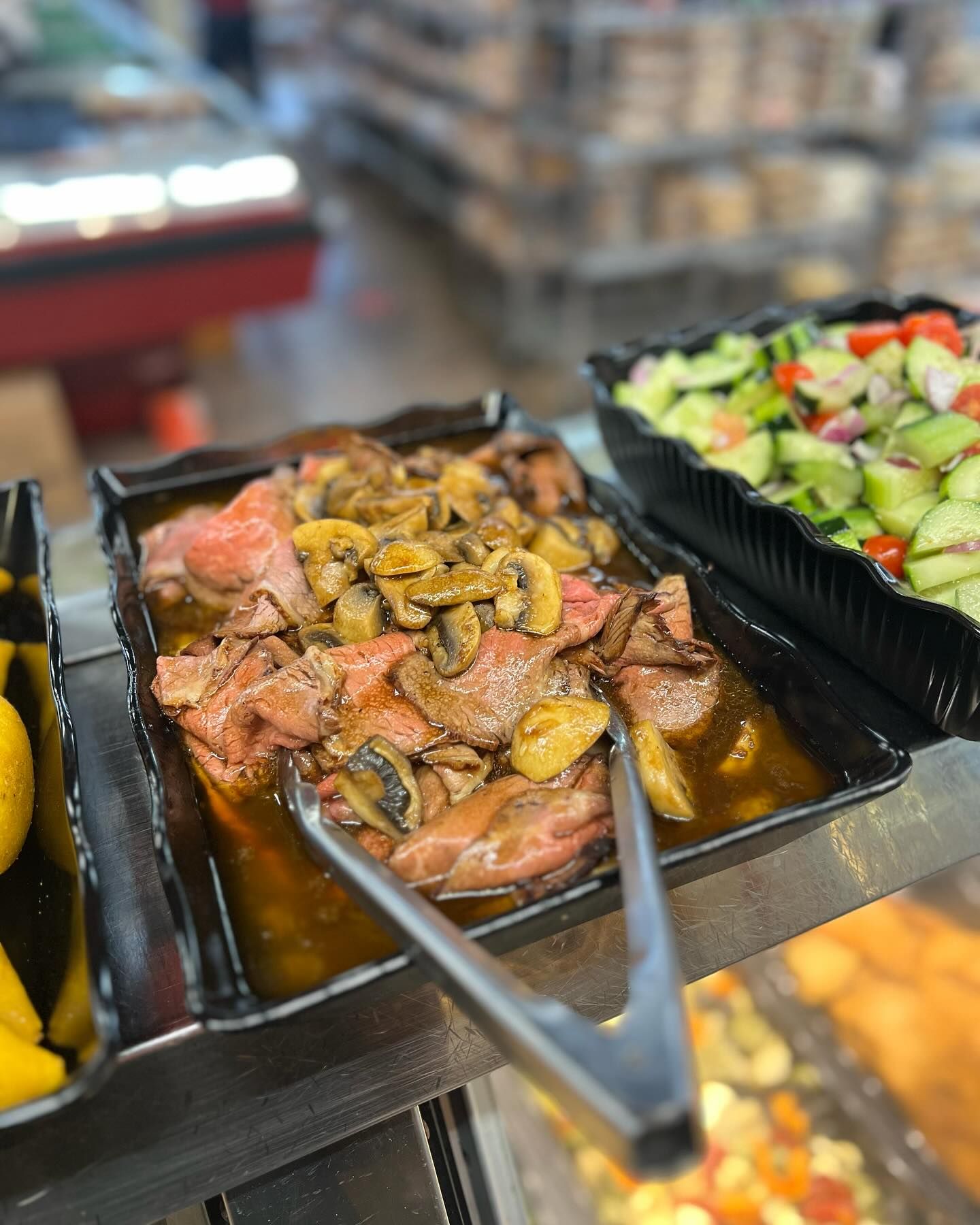 A tray of roast beef with mushrooms and tongs on a table.