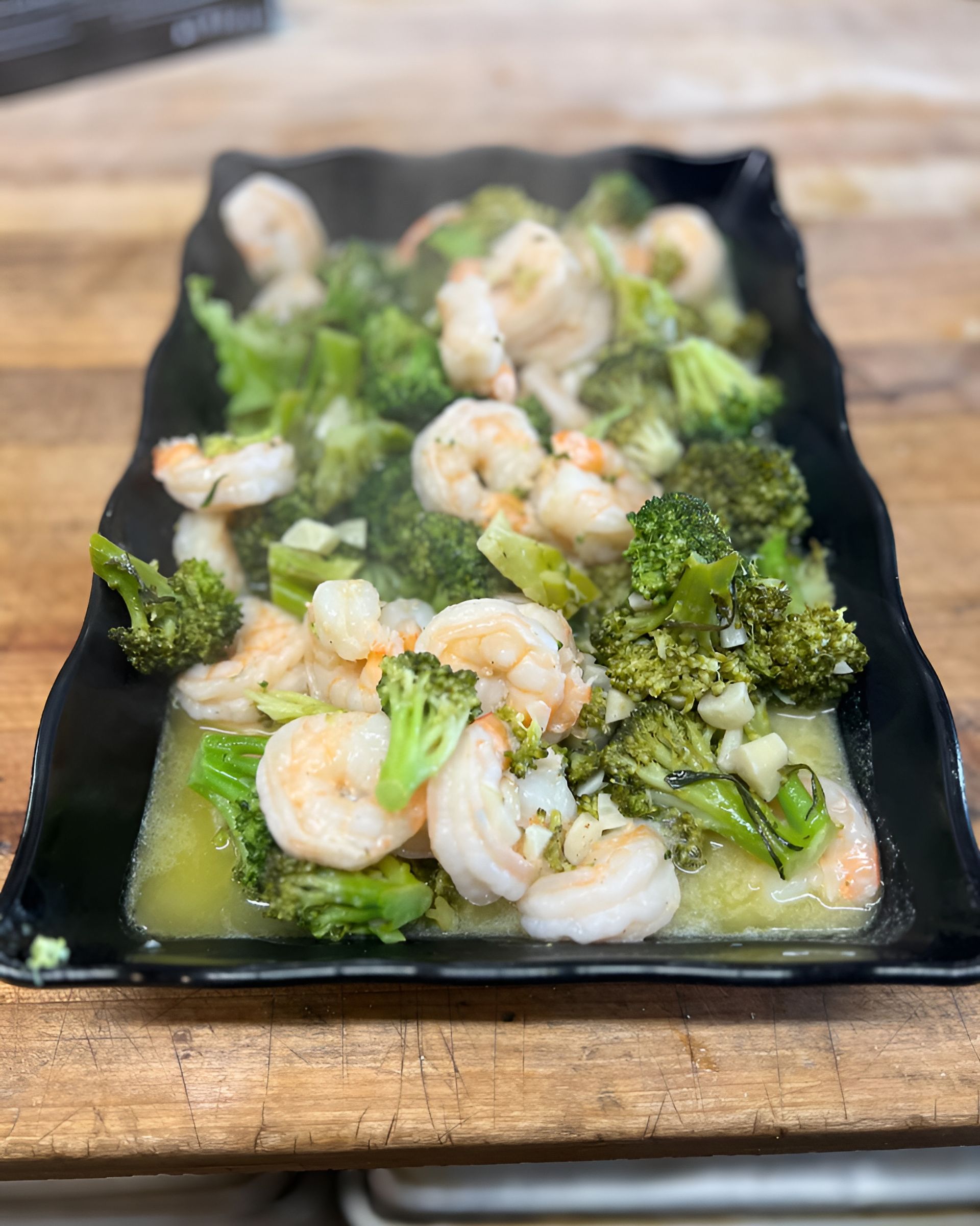 A black plate topped with shrimp and broccoli.