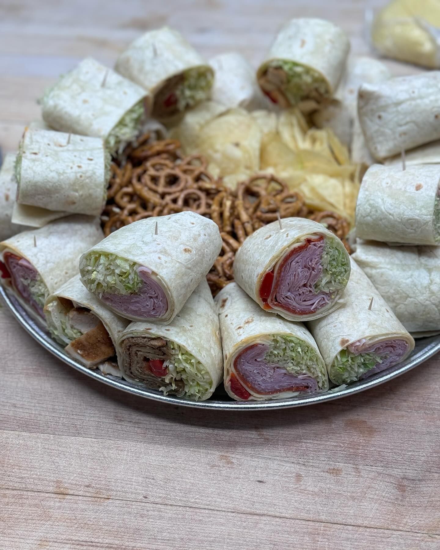 A tray of wraps and pretzels on a wooden table.