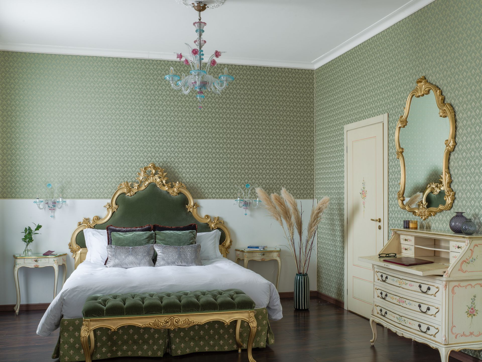 Elegant green-and-gold bedroom with ornate bed, dresser, mirror, and chandelier