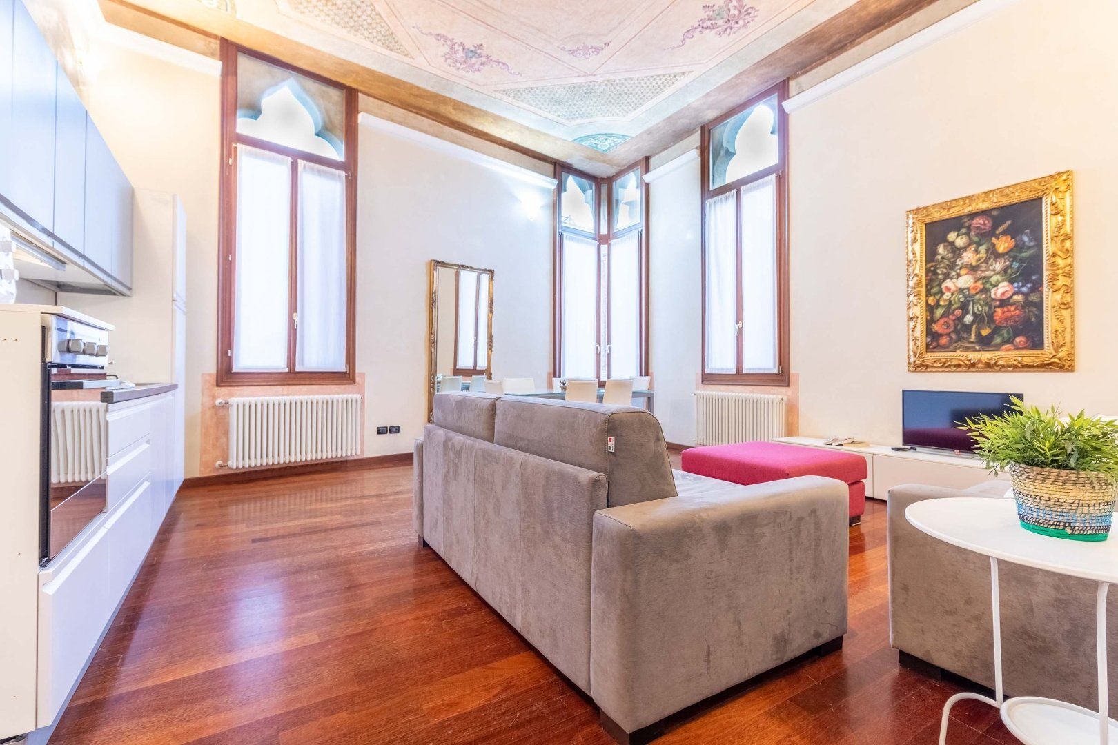 Bright modern living room with large windows, hardwood floors, gray sofa, and colorful wall art