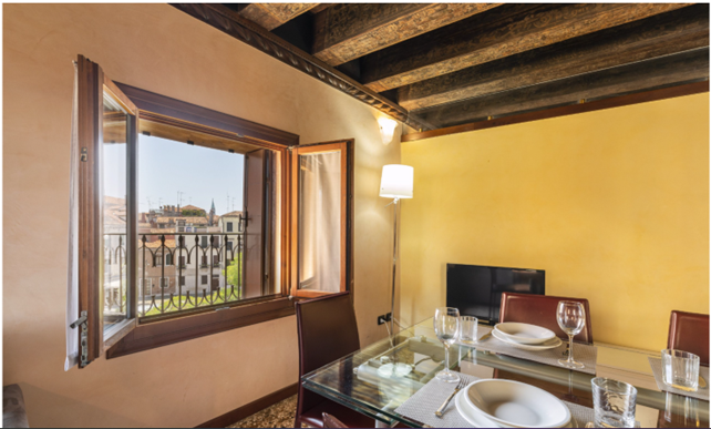 Dining room with open window, rustic ceiling beams, yellow wall, and a set dining table overlooking a city view