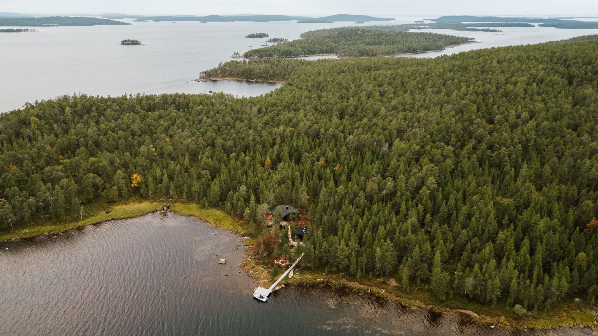 Forest island and shoreline with small dock. Lake water and distant islands.
