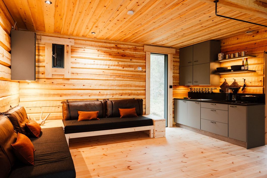 A living room with a couch and a kitchen in a log cabin.