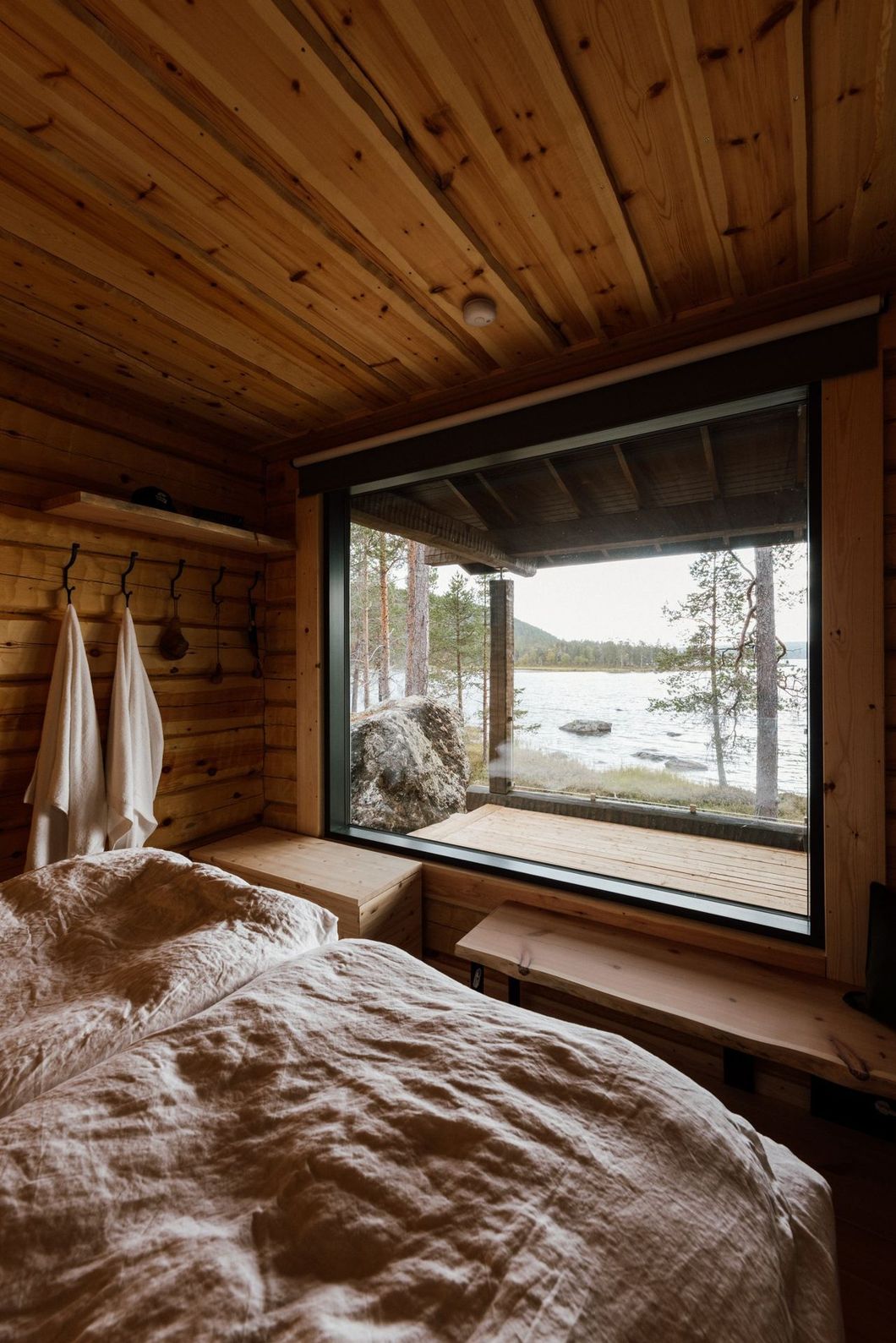 A bedroom in a log cabin with a large window overlooking a lake.