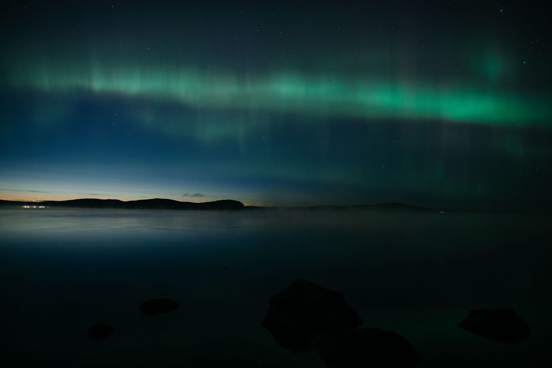 An aerial view of a body of water with a rock in the middle and a person fly fishing in the water