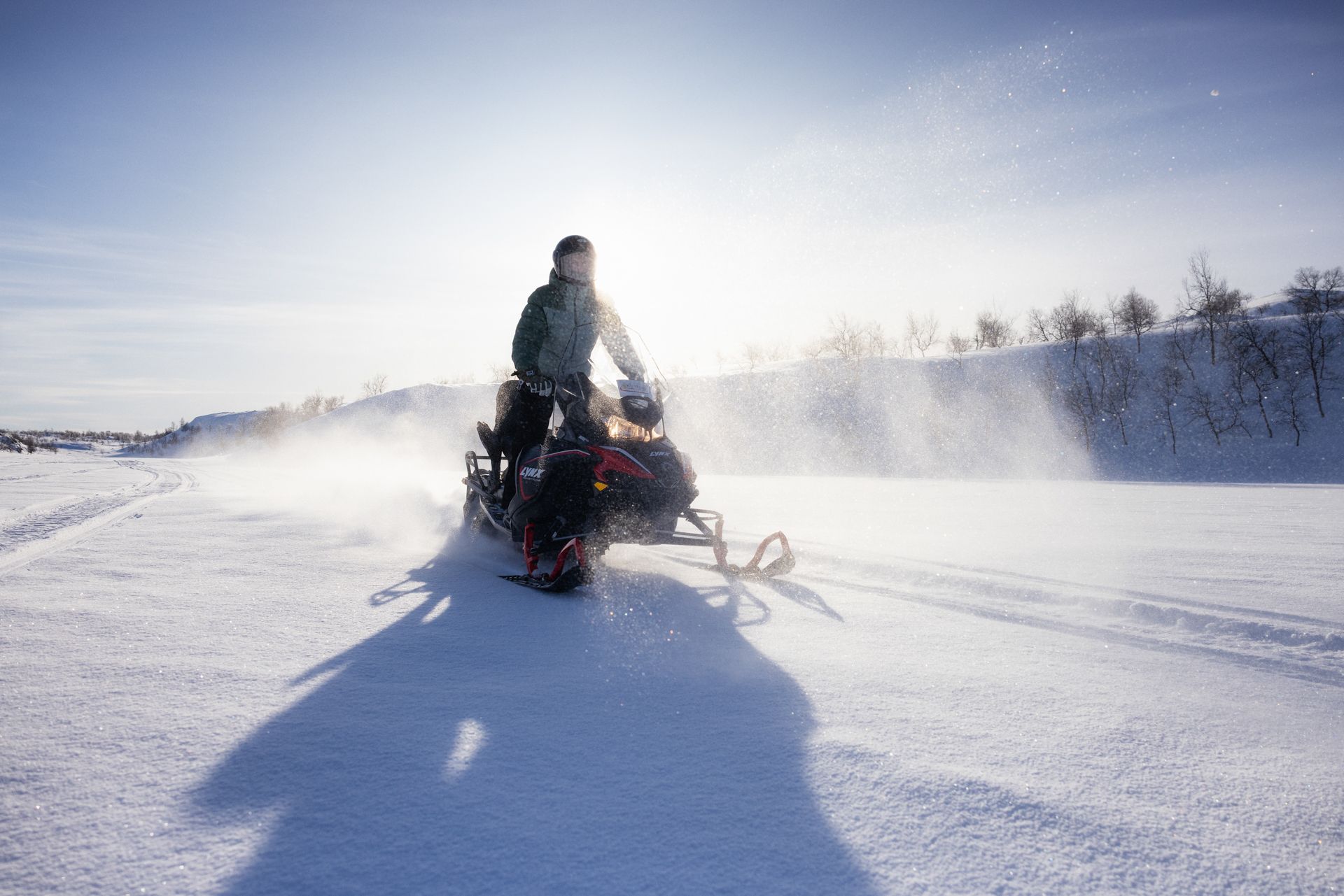 Person riding snowmobile across a snow-covered landscape on a sunny day.