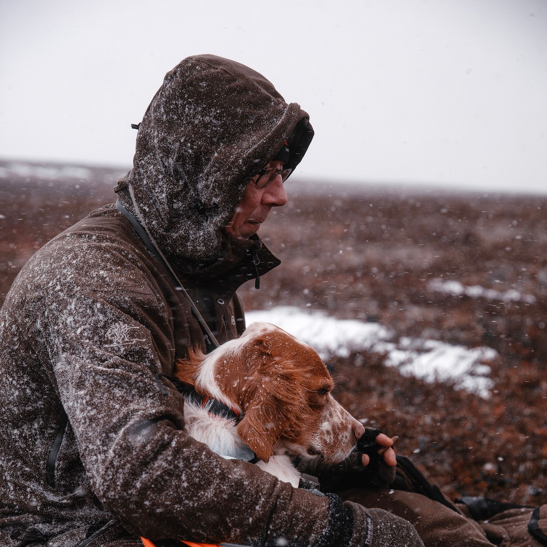 A man in a hooded jacket is holding a small dog