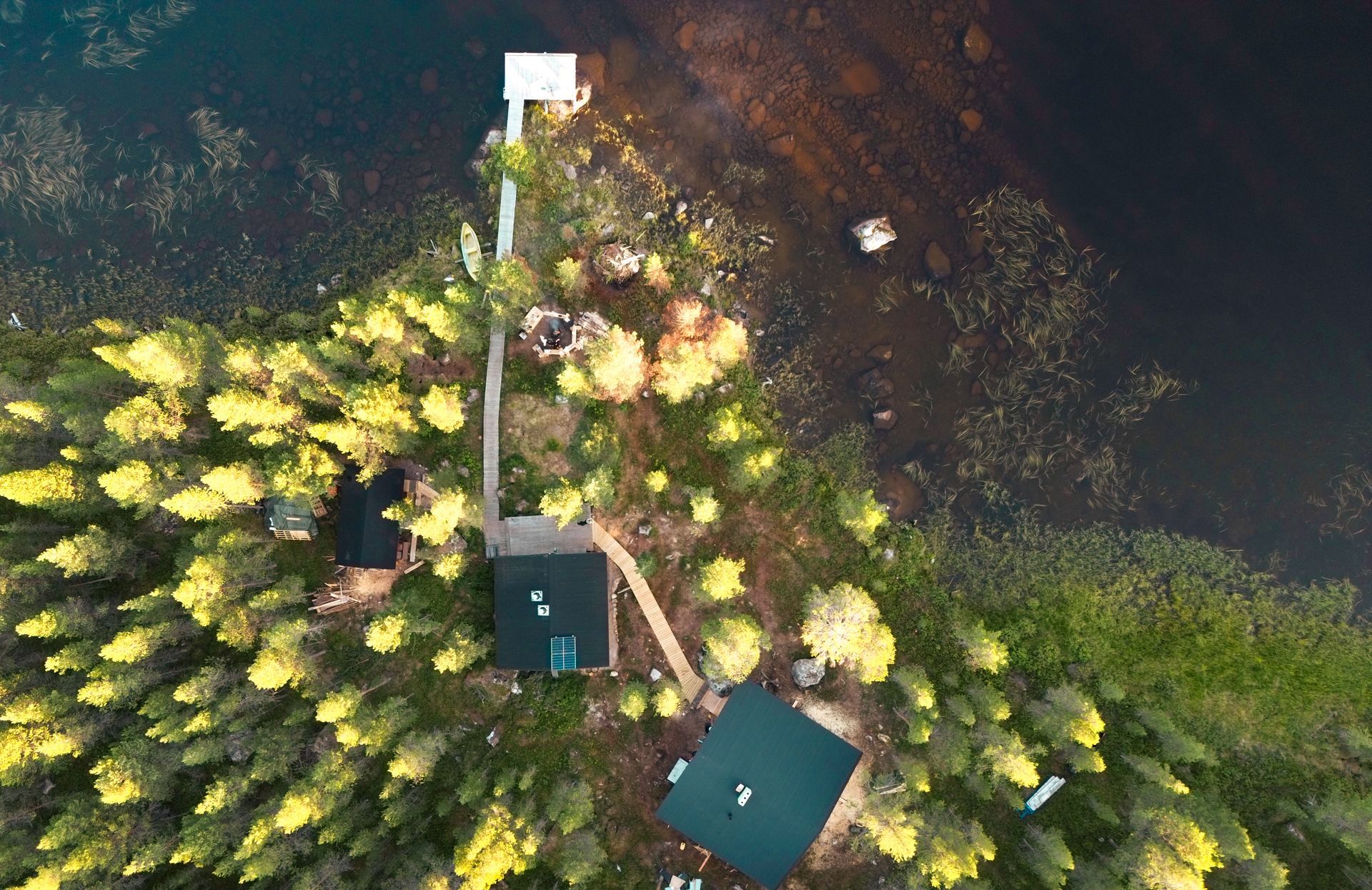An aerial view of a house in the middle of a forest next to a lake.