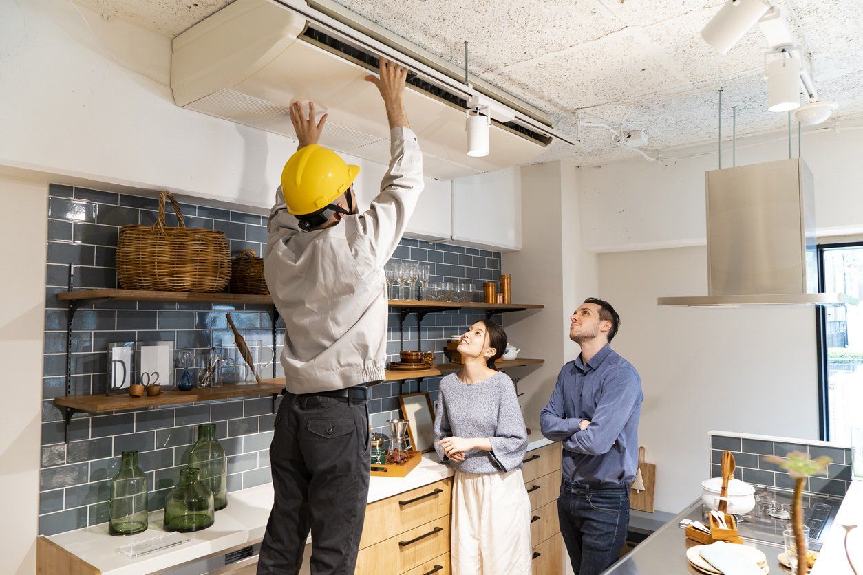 A man is installing an air conditioner in a kitchen while a woman looks on.