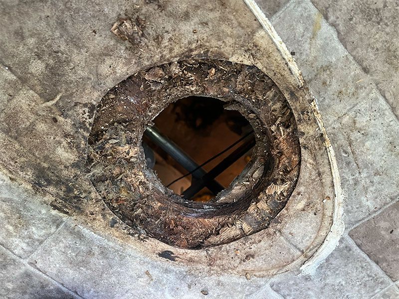 Ceiling hole with damaged edges, exposing pipes below. Dark debris surrounds the opening.