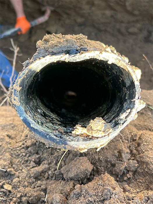 A section of a dark pipe with rough, light-colored edges, viewed from inside, surrounded by brown soil.