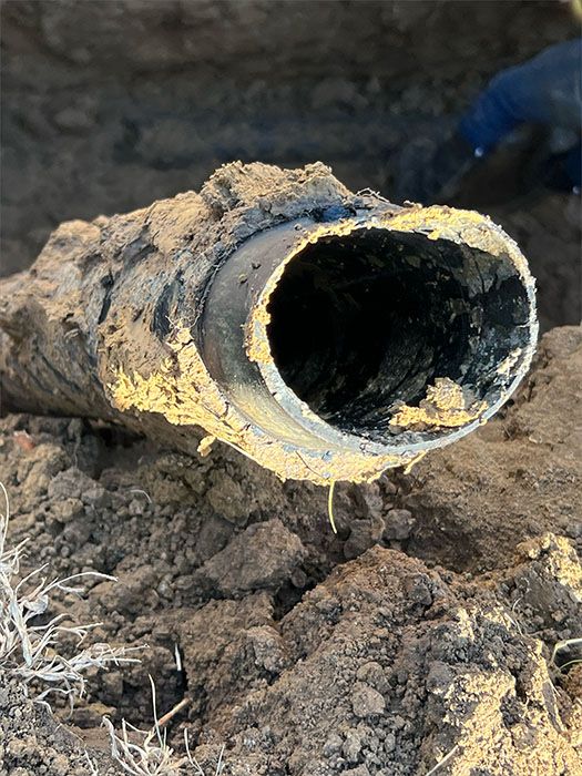 A cut black pipe, coated in mud, in an excavated area.