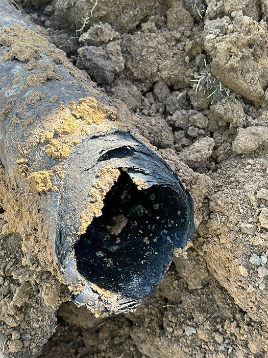 Damaged black pipe in dirt, showing a large hole.