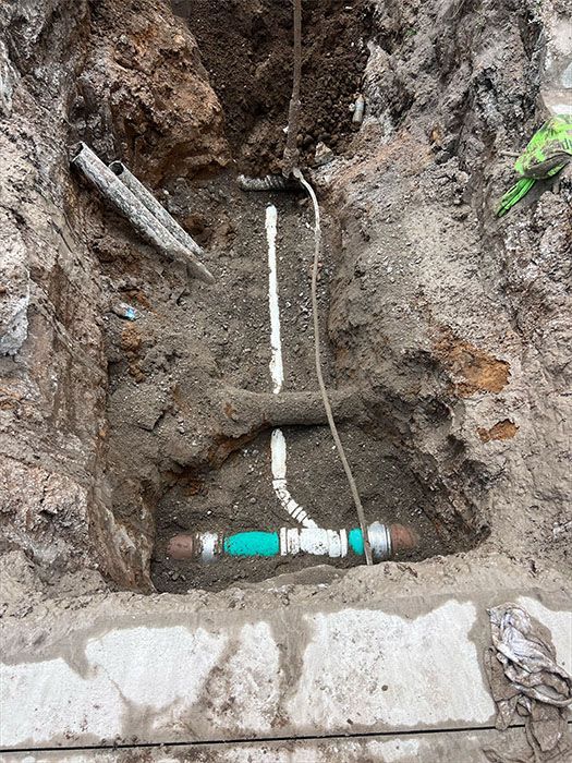 Pipes and fittings in an excavated hole, with a central white pipe and a green section.