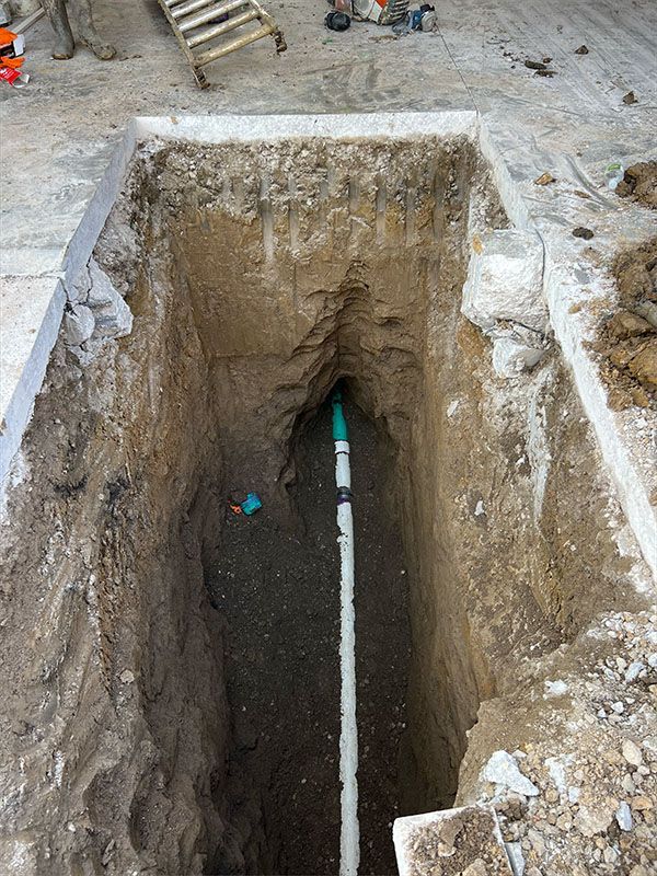A deep rectangular trench with a white pipe running through it, likely for plumbing work.