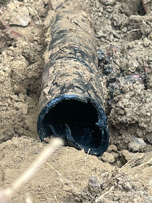 Black pipe, cracked and broken, exposed in brown soil.