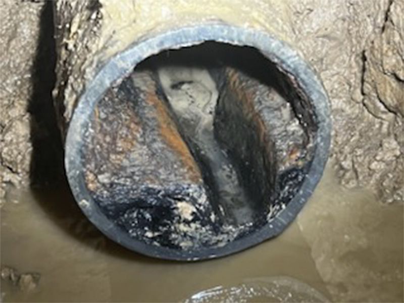 A clogged pipe filled with debris, viewed from inside, surrounded by murky water.