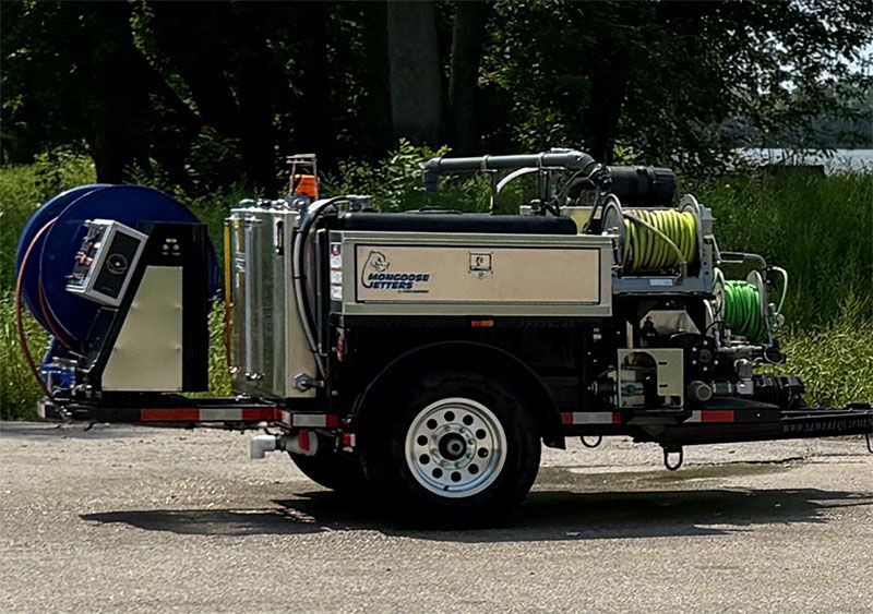 Trailer-mounted hydro-excavation unit with tanks, reels, and equipment, parked on pavement.