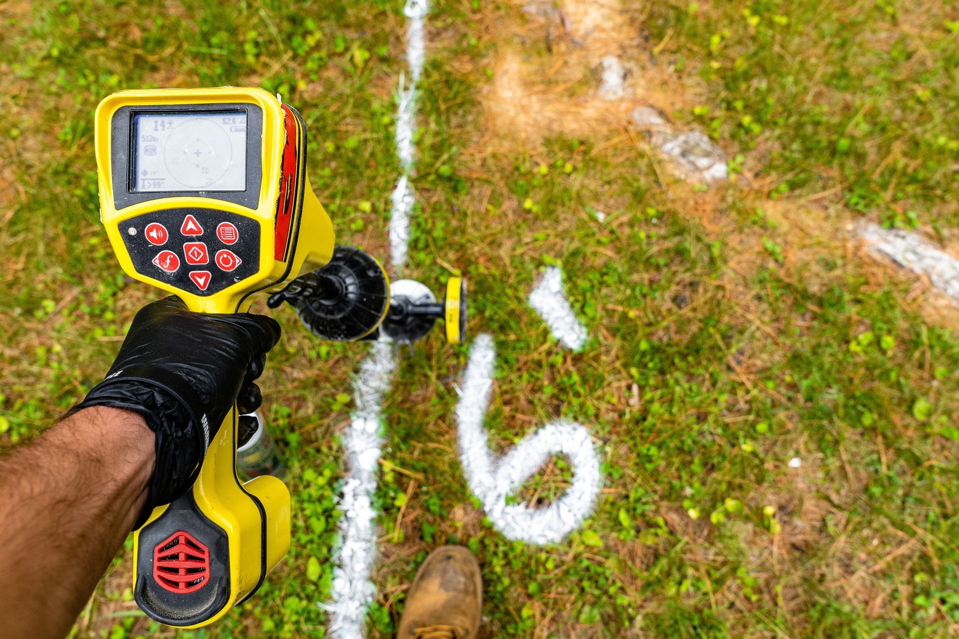 A person holding a yellow utility locator on grass, marking a 