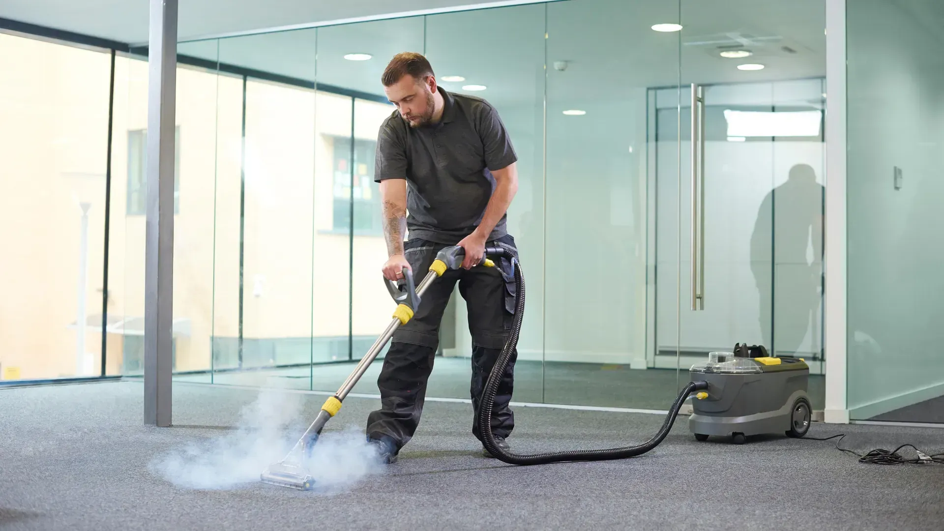 A man is using a vacuum cleaner to clean a carpet in an office.