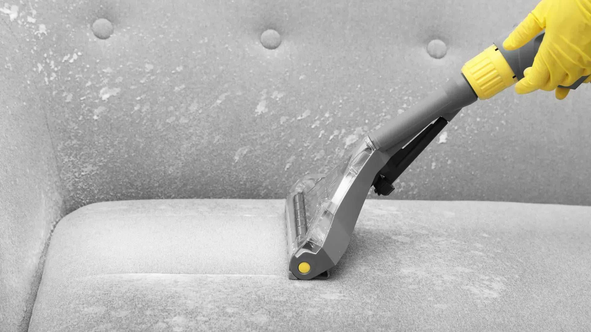 A person is cleaning a couch with a vacuum cleaner.