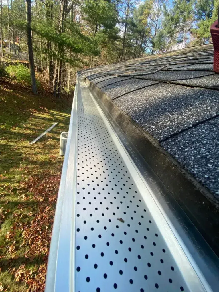 A close up of a gutter on a roof with trees in the background.