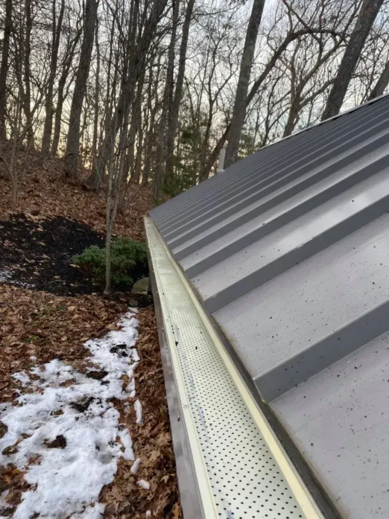 A close up of a gutter on a roof with trees in the background