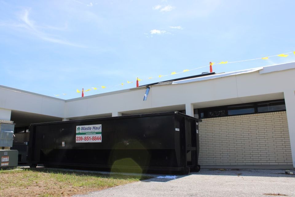 Black dumpster beside a white industrial building with a closed garage door and a small sign on the dumpster