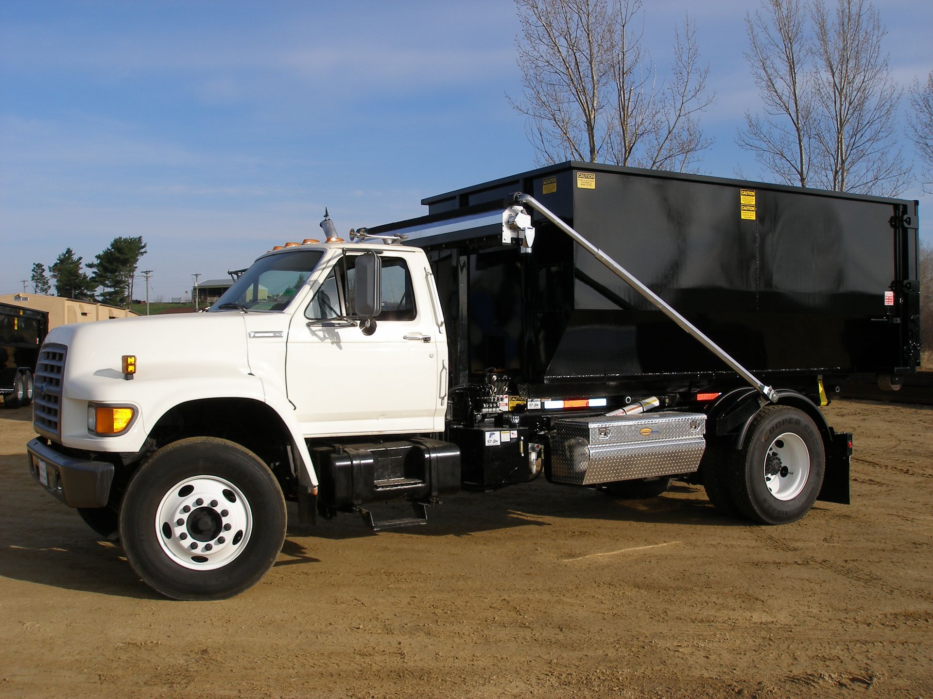 White dump truck with black bed parked on a dirt lot under a blue sky