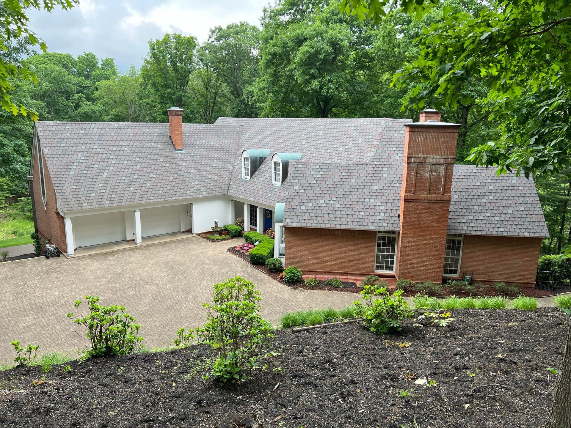 A large brick house with a gray roof is surrounded by trees.
