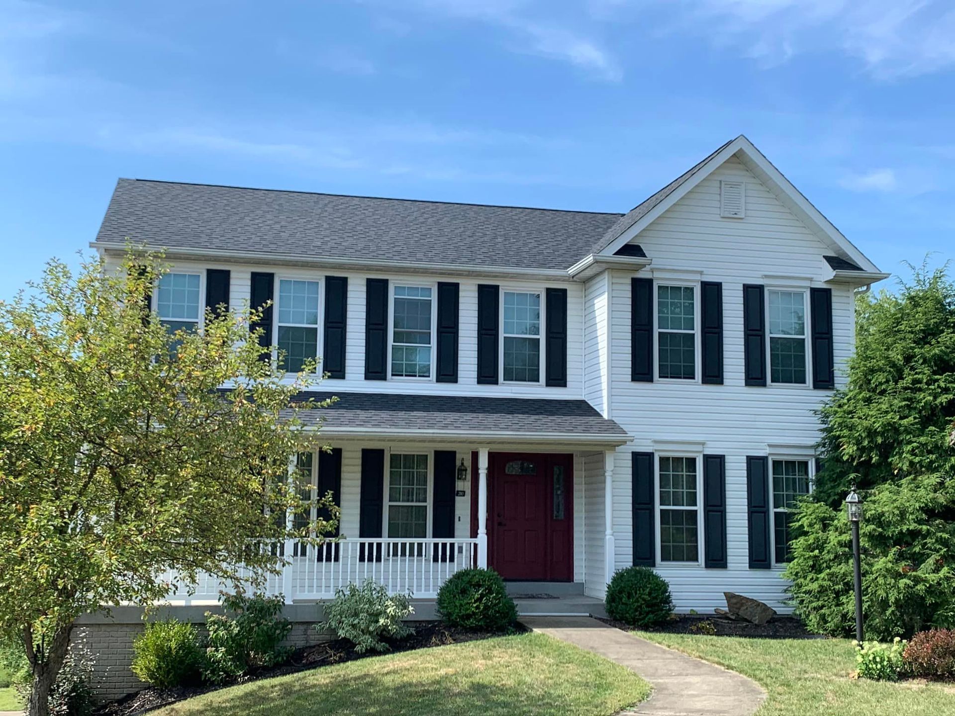A large white house with black shutters and a red door.