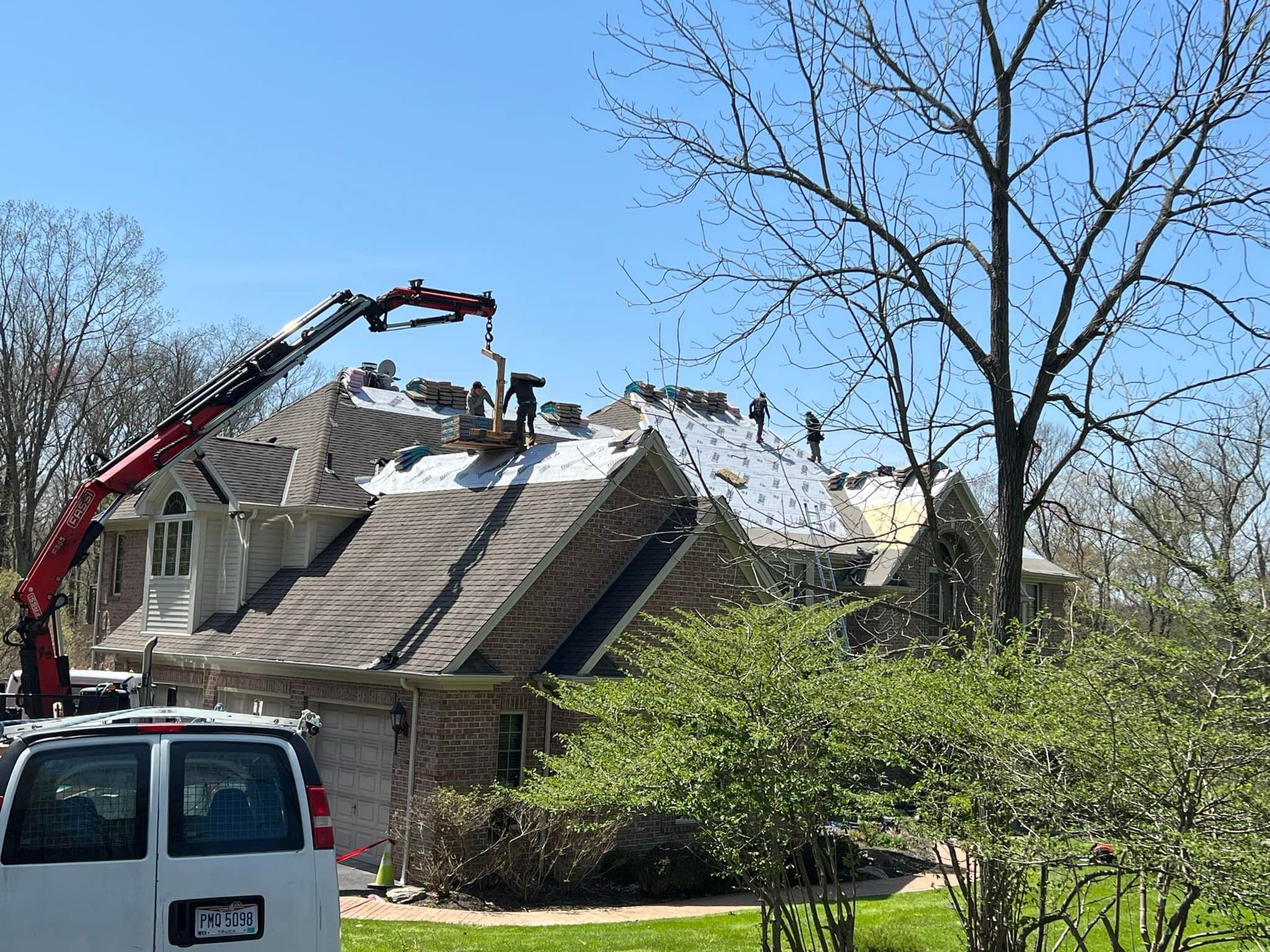 A white van is parked in front of a house with a crane on the roof.
