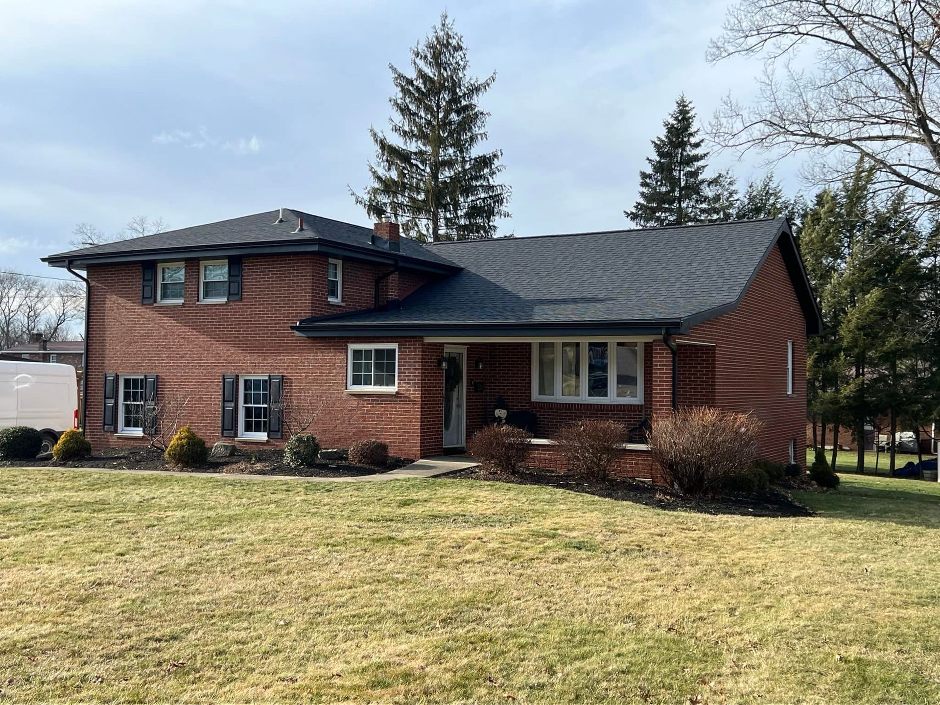 A large brick house with a black roof is sitting on top of a lush green field.