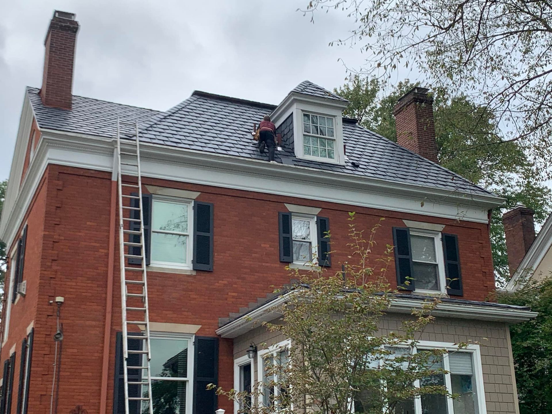 A man is standing on the roof of a large brick house.
