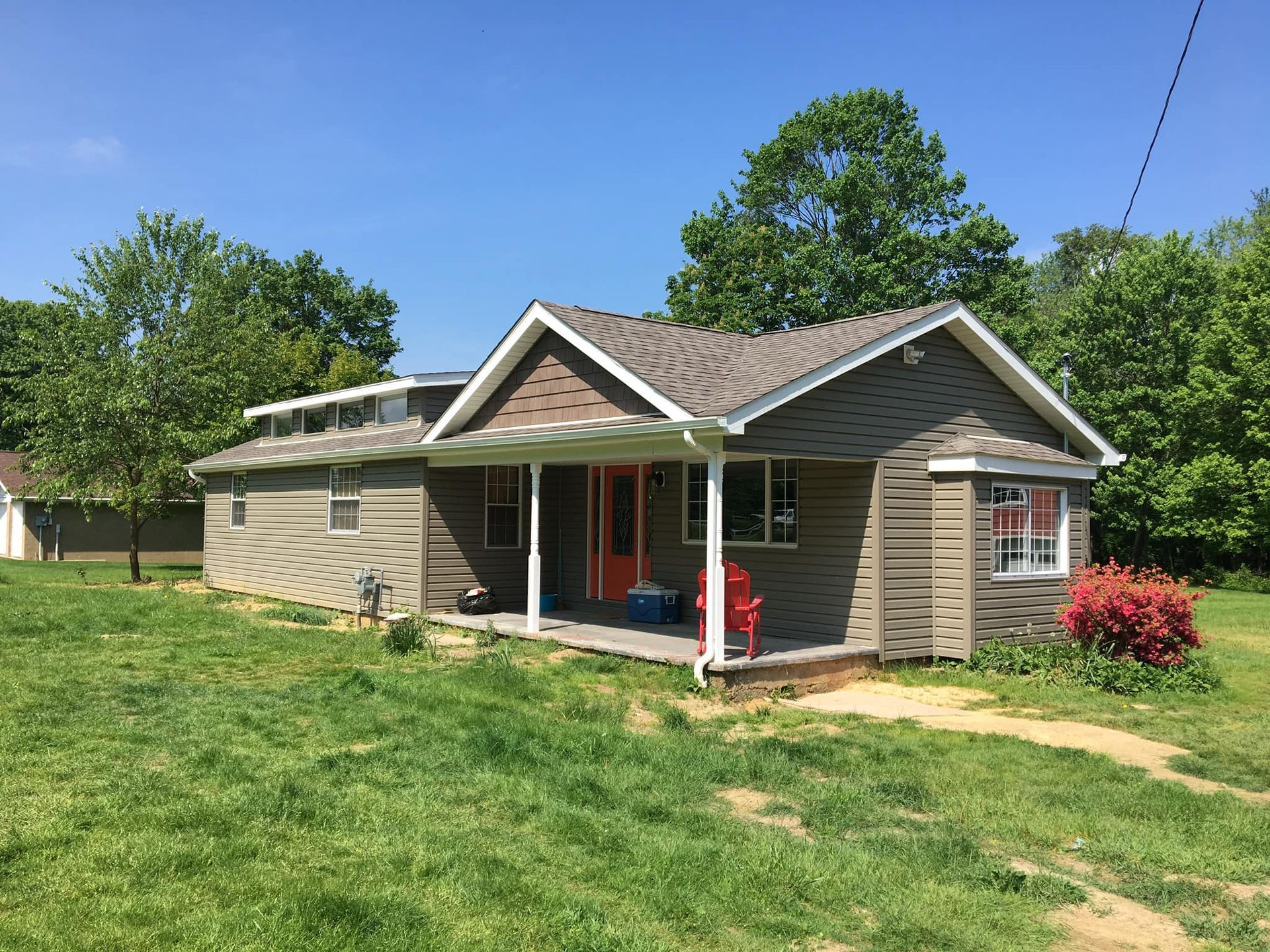 A small house with a porch in the middle of a grassy field.