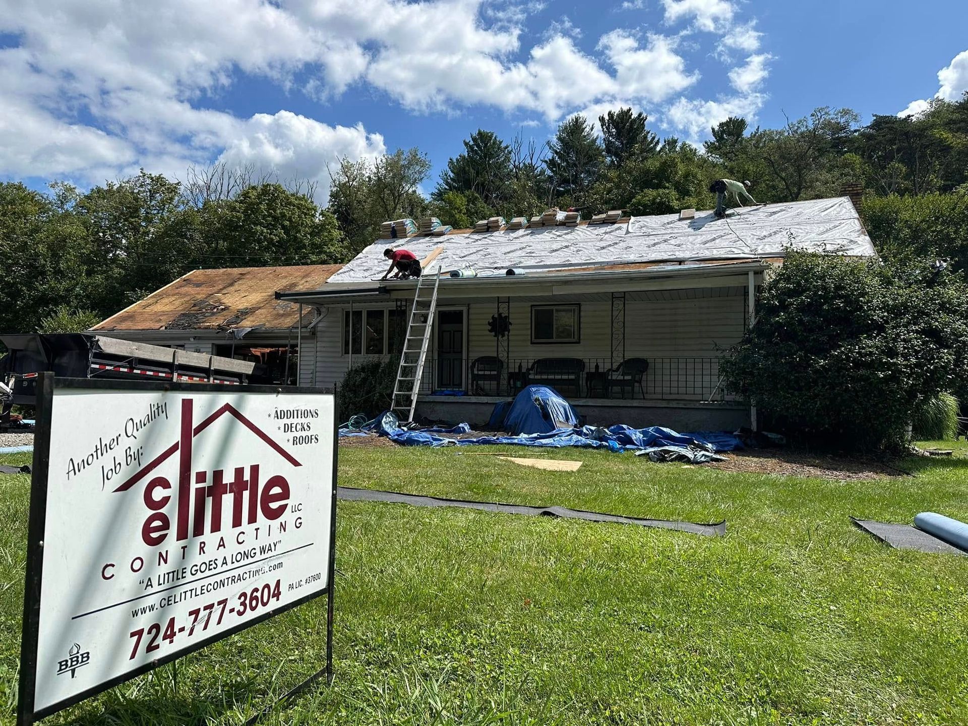 A man is working on the roof of a house with a sign in front of it.