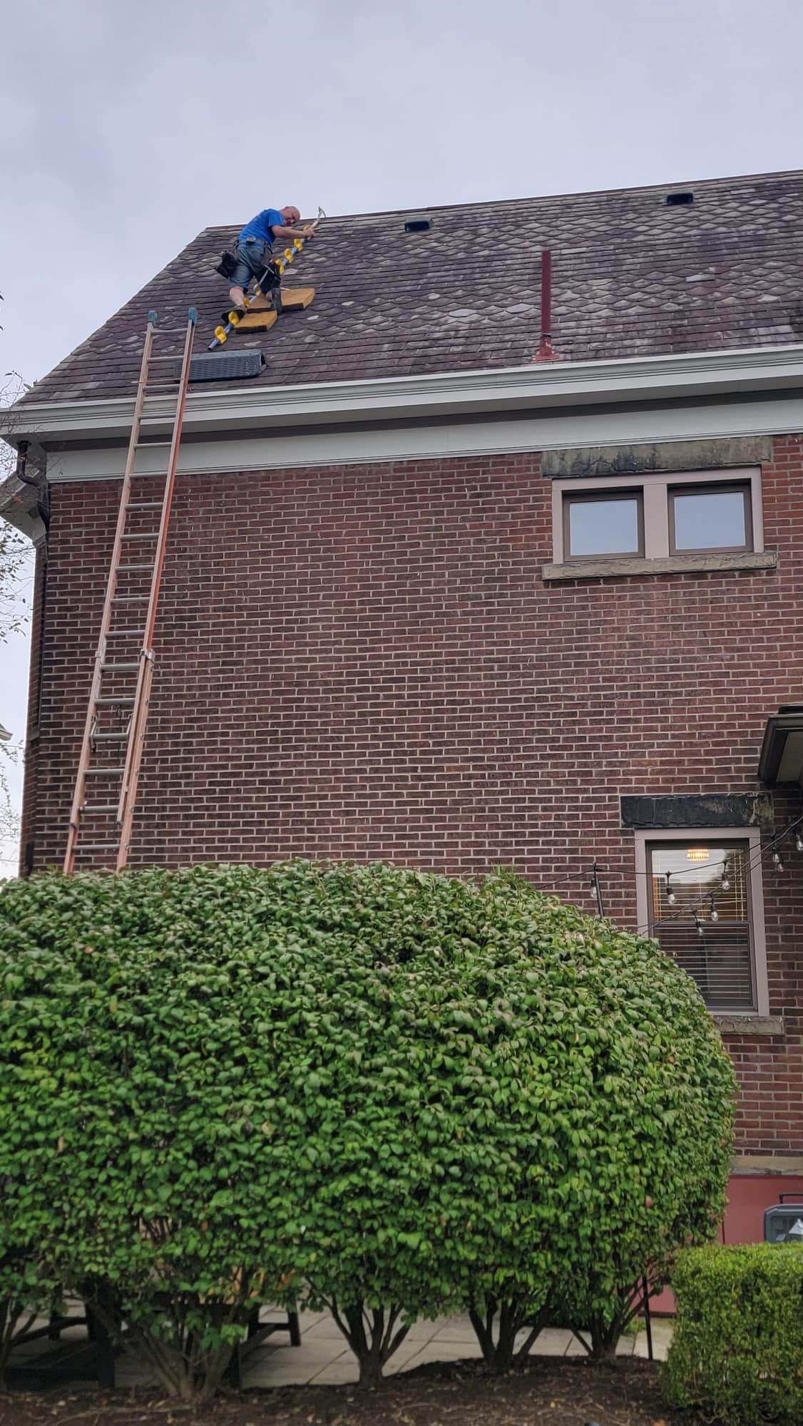 A man is working on the roof of a brick house.