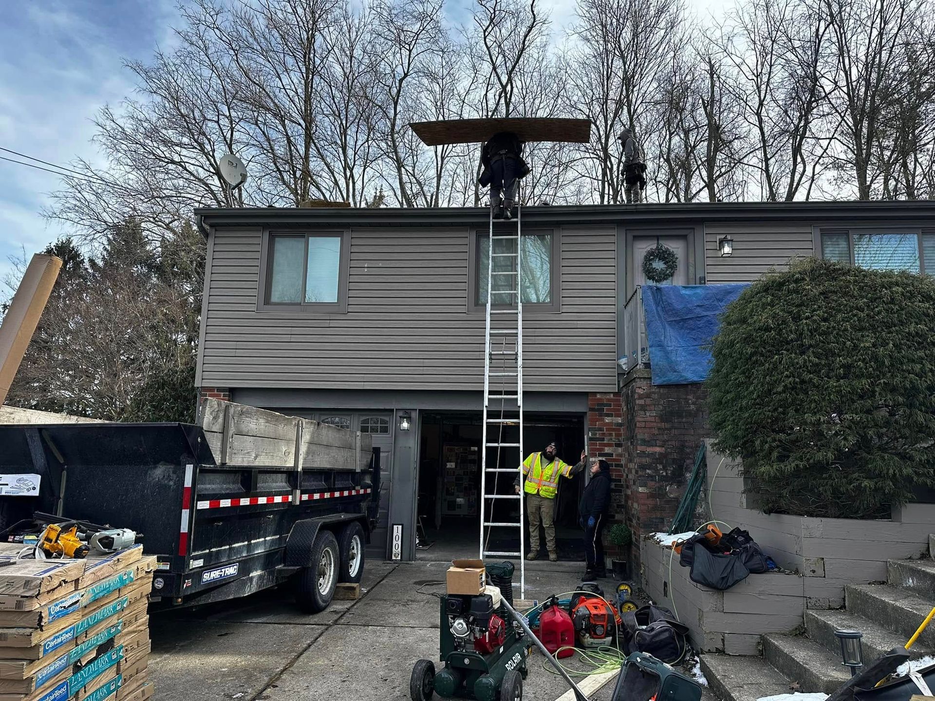 A man on a ladder is working on the roof of a house.