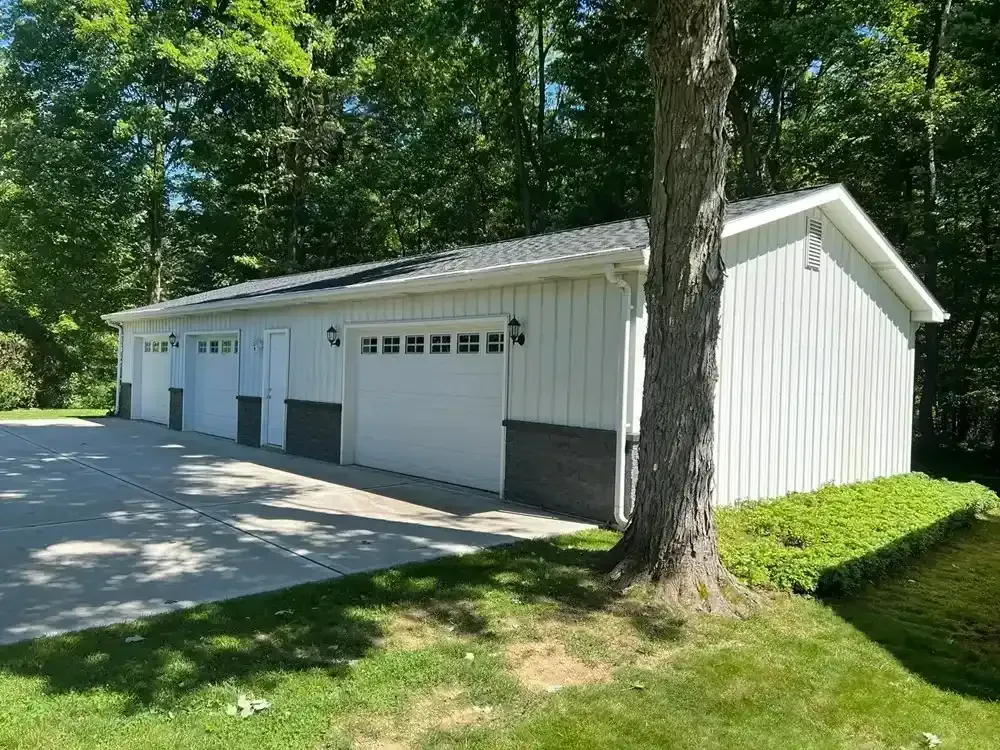 A white garage with a tree in front of it.