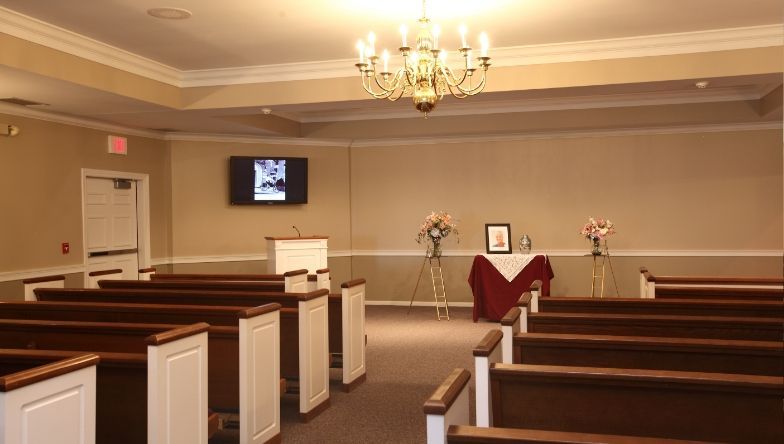 An empty church with rows of wooden benches and a chandelier.