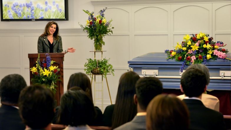 A woman is giving a speech at a funeral in front of a coffin.