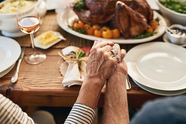 A couple is holding hands at a table with a turkey on it.