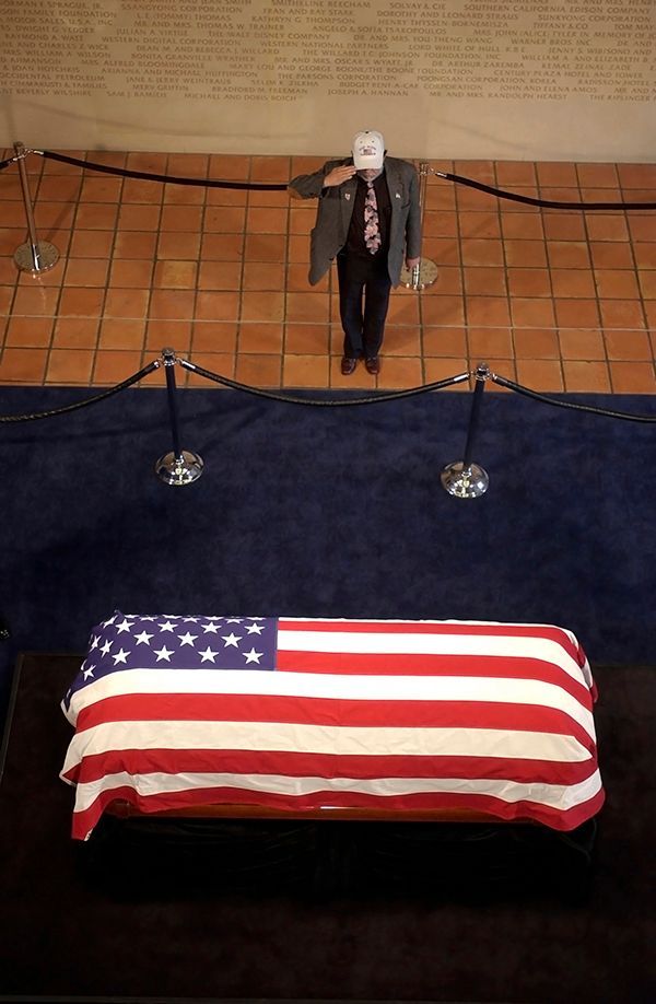 a man salutes in front of an american flag draped coffin