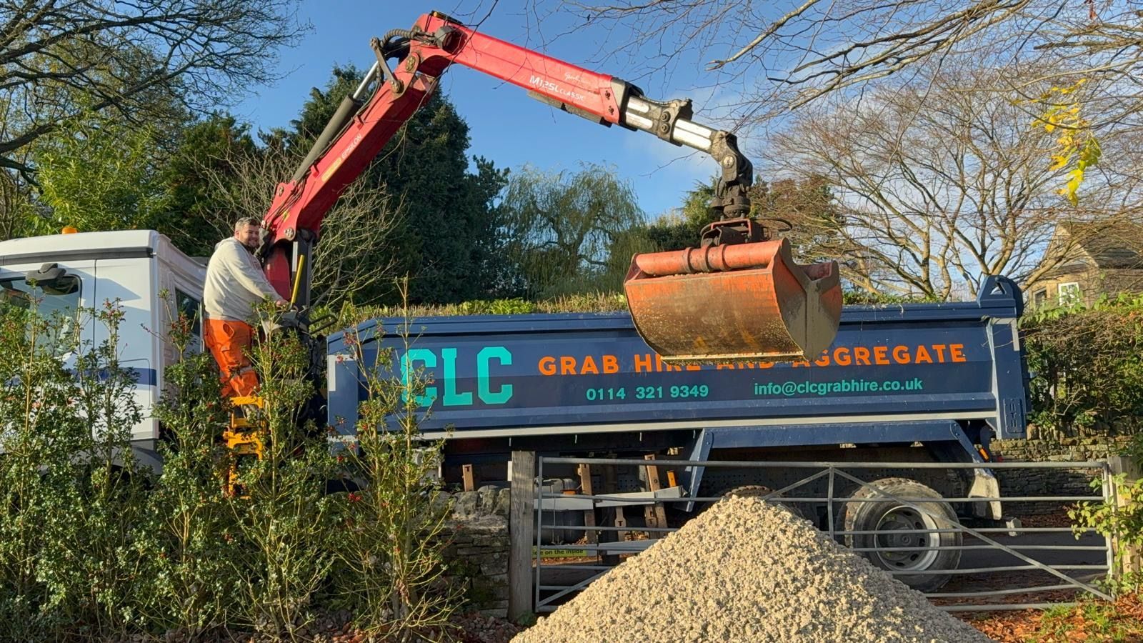 A worker operating a truck-mounted crane loading gravel into the truck bed.