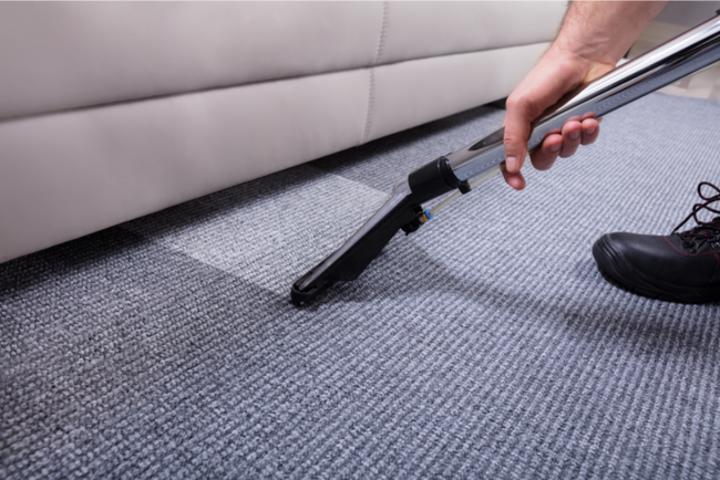 Person vacuums a blue carpet near a beige couch.
