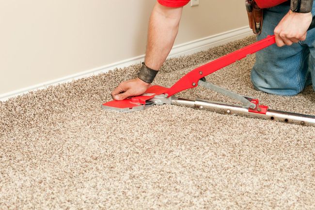Person using a utility knife to trim carpet edge with a guide, indoors.