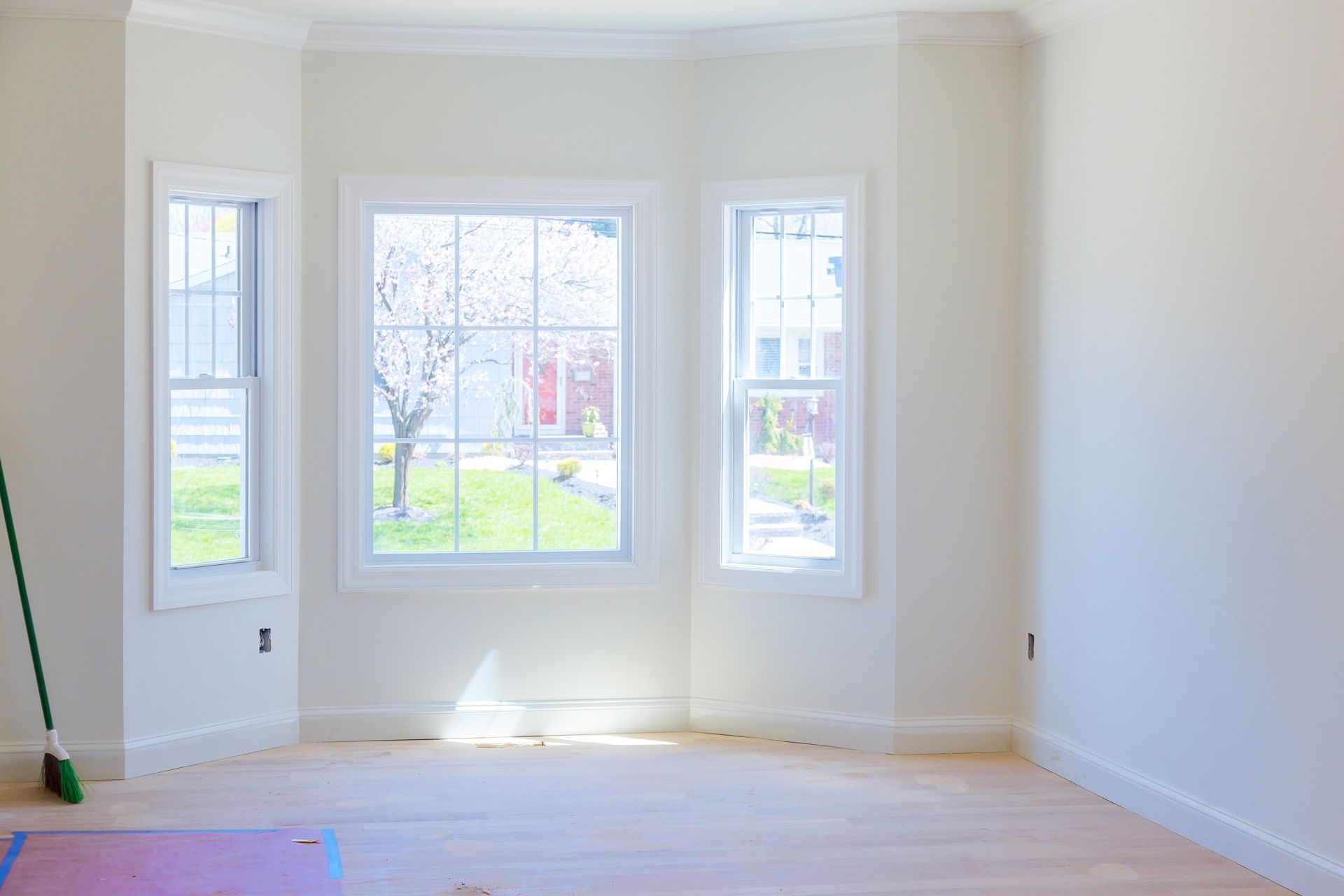 Empty bright room with three tall windows, white walls, and light wood floors