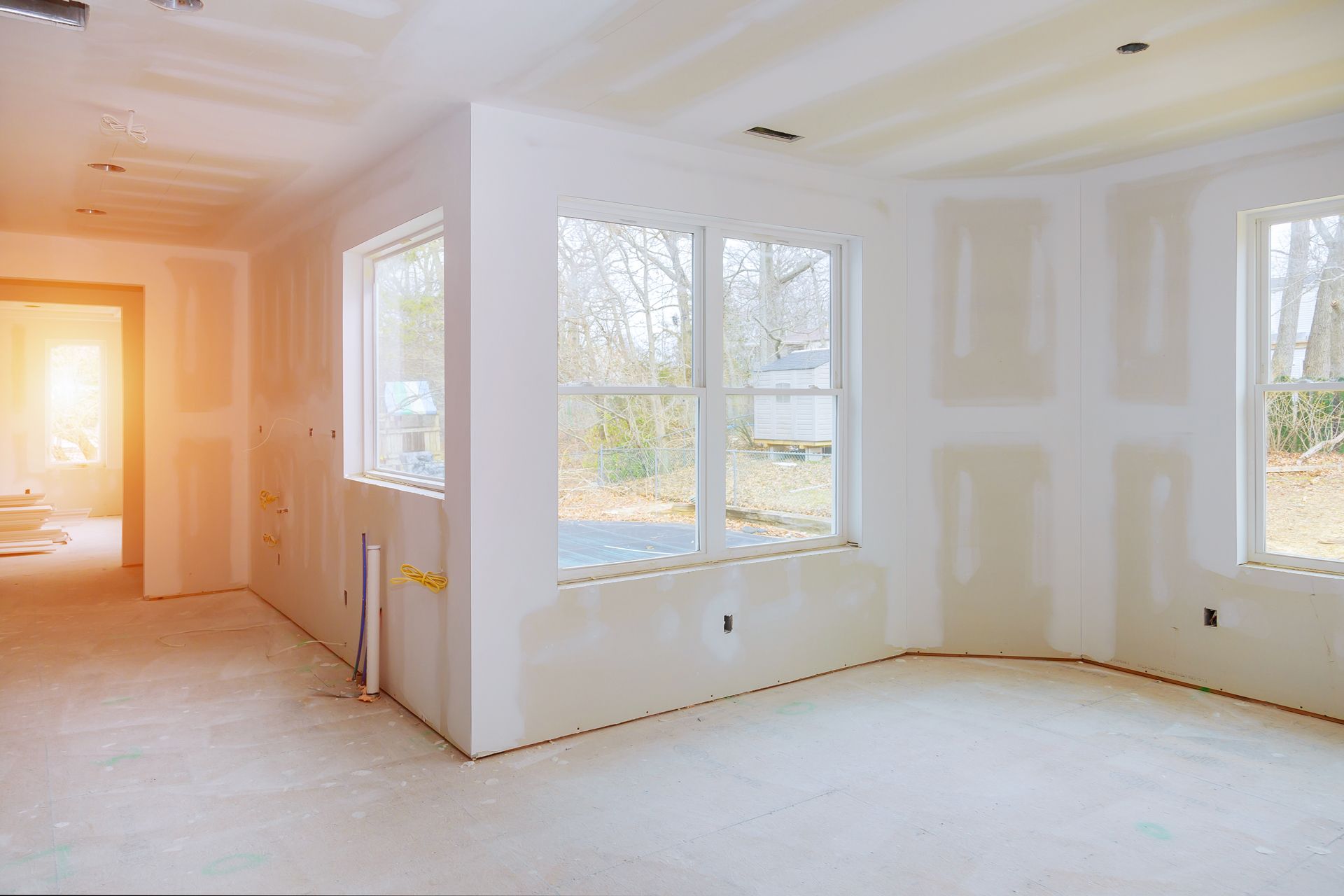 Bright unfinished room with white walls, large windows, and sunlight streaming in